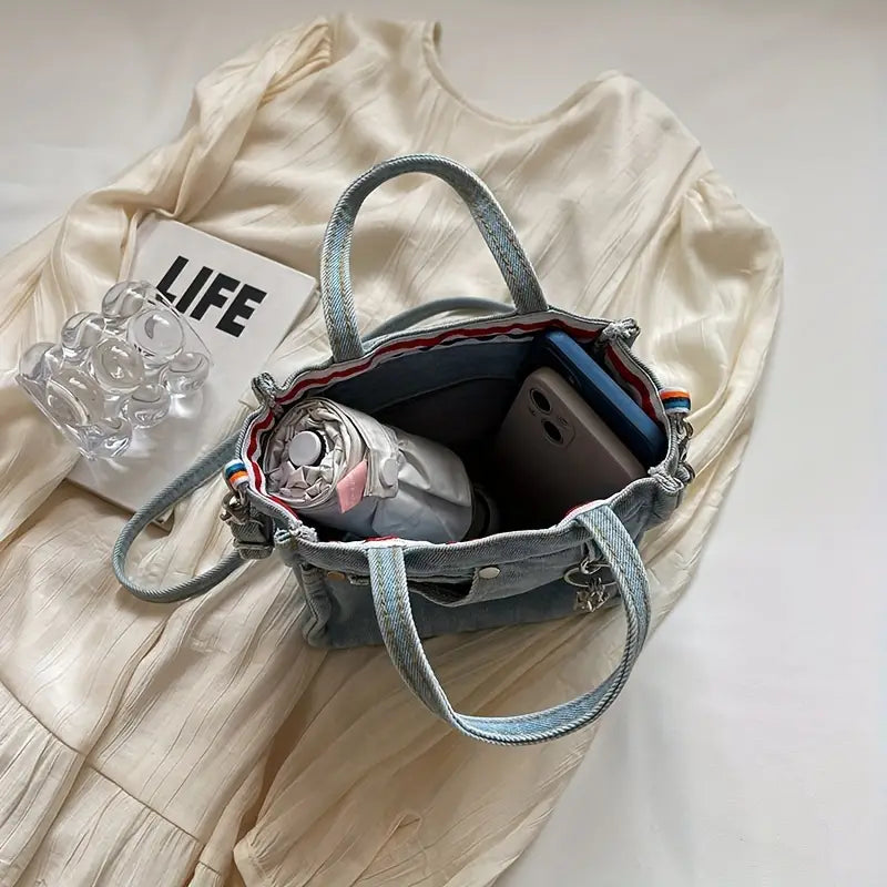Borsa in denim con manici, contenente smartphone, bottiglia d'acqua e libro su abito bianco. Accessori moda donna, stile casual chic.