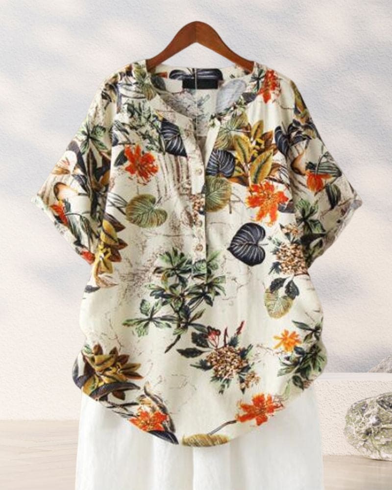 Camicia donna floreale in cotone, maniche corte, sfondo bianco, stampa tropicale colorata, casual estiva, bottoni frontali, appesa su gruccia.