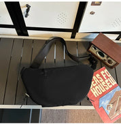 Borsa a tracolla nera su panca grigia, accanto a una radio vintage e una rivista. Design moderno, ideale per moda urbana e viaggi.
