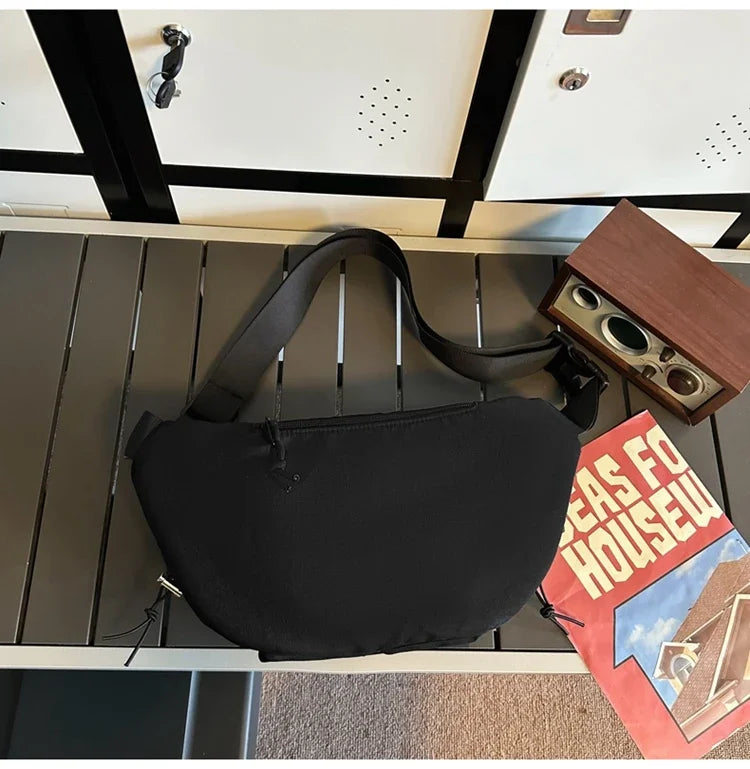 Borsa a tracolla nera su panca grigia, accanto a una radio vintage e una rivista. Design moderno, ideale per moda urbana e viaggi.