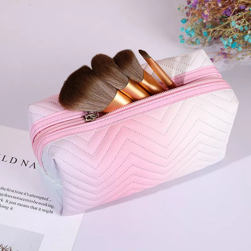 Astuccio per trucchi rosa sfumato con motivo a zigzag, contenente pennelli da trucco con manico dorato. Accessorio cosmetico elegante e pratico.