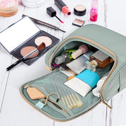 Beauty case verde aperto su tavolo bianco, contenente cosmetici, pennelli trucco, specchio e prodotti skincare. Organizzatore da viaggio elegante e pratico.