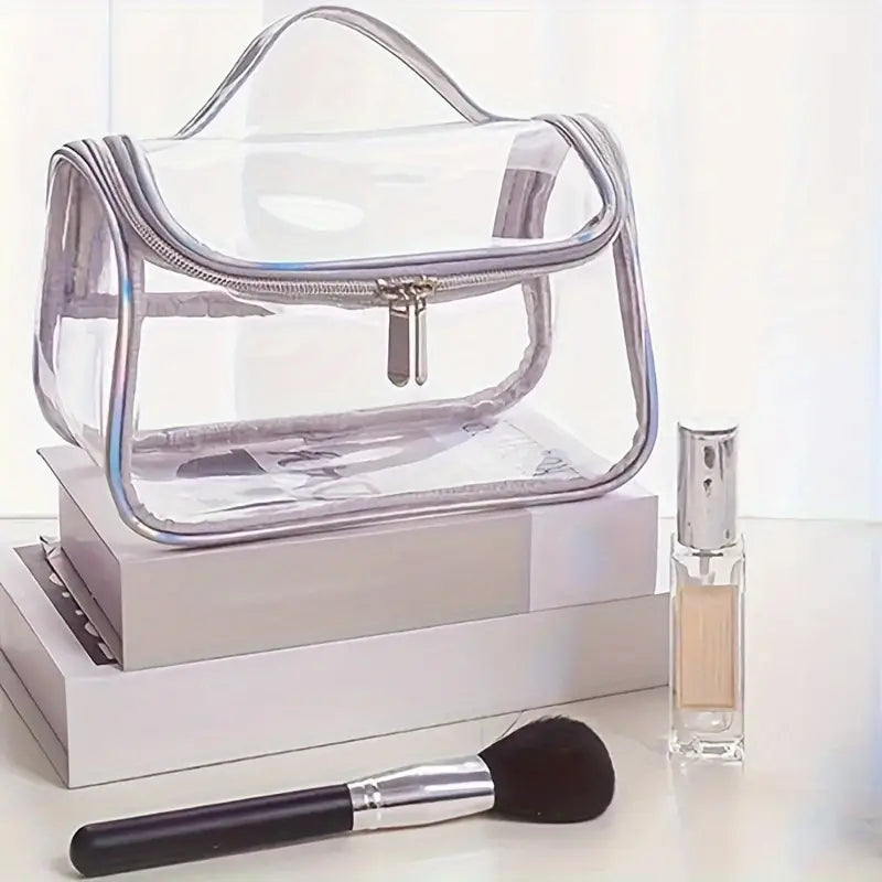 Borsa trasparente in PVC con cerniera, posizionata su libri, accanto a pennello da trucco e flacone di profumo. Accessori moda e bellezza.