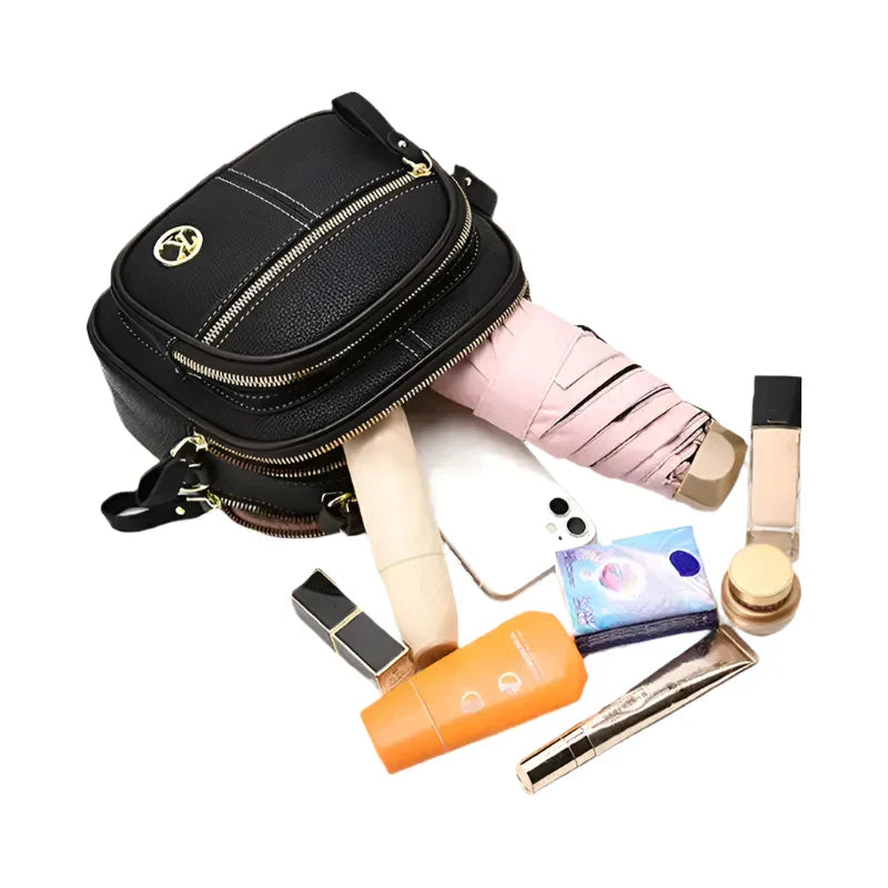 Borsa a tracolla nera in pelle con cerniere dorate, contenente cosmetici, ombrello rosa e smartphone. Accessori moda donna eleganti e pratici.