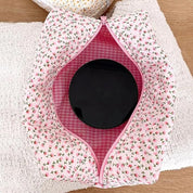 Astuccio cosmetico rosa con motivo floreale, aperto per mostrare l'interno a quadretti rosa e contenente un barattolo nero. Accessorio da viaggio elegante.
