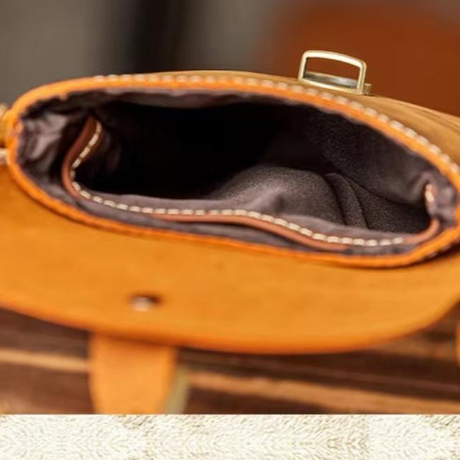 Borsa a tracolla in pelle marrone aperta, vista dall'alto. Interno foderato in tessuto scuro. Elegante accessorio moda per uomo e donna.
