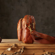 Borsa a tracolla in pelle marrone con cerniere dorate, design vintage, su tavolo di legno. Accessorio moda uomo, stile retrò elegante.