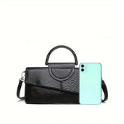 Borsa a mano in pelle nera con texture serpente, elegante e moderna, accanto a uno smartphone verde chiaro. Accessorio moda donna di lusso.