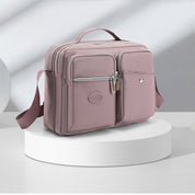 Borsa a tracolla rosa da donna su piedistallo bianco, design elegante con tasche multiple e cerniere, ideale per moda e praticità quotidiana.