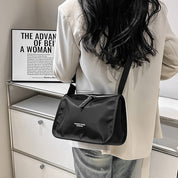 Donna con borsa a tracolla nera in nylon, indossa giacca bianca. Design moderno, ideale per moda urbana. Sfondo con poster motivazionale.