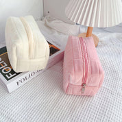 Due astucci in tessuto trapuntato, uno bianco e uno rosa, su un tavolo con lampada e libro. Design elegante, ideale per cosmetici o accessori.