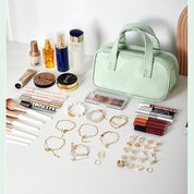 Borsa cosmetica verde con trucchi, pennelli, gioielli e rossetti su tavolo bianco. Accessori bellezza, organizzazione trucco, set make-up.
