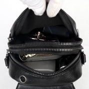 Zaino in pelle nera aperto, mostra scomparti con cerniere, chiavi e accessori all'interno. Design elegante, ideale per moda e praticità quotidiana.