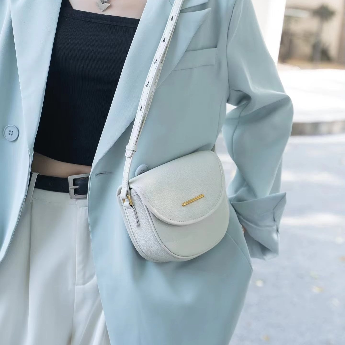 Giacca azzurra elegante con borsa a tracolla bianca in pelle, abbinata a top nero e pantaloni chiari. Moda donna, accessori di tendenza.
