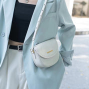 Giacca azzurra elegante con borsa a tracolla bianca in pelle, abbinata a top nero e pantaloni chiari. Moda donna, accessori di tendenza.