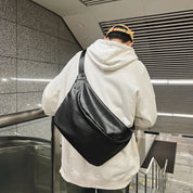 Uomo con felpa bianca e cappellino beige indossa borsa a tracolla nera in pelle, stile urbano, su scala mobile in metropolitana moderna.