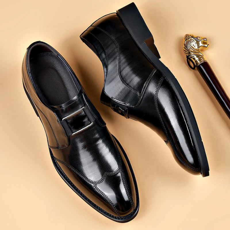 Scarpe eleganti uomo in pelle nera lucida, stile classico, con fibbia. Ideali per abbigliamento formale. Sfondo beige con bastone decorativo.