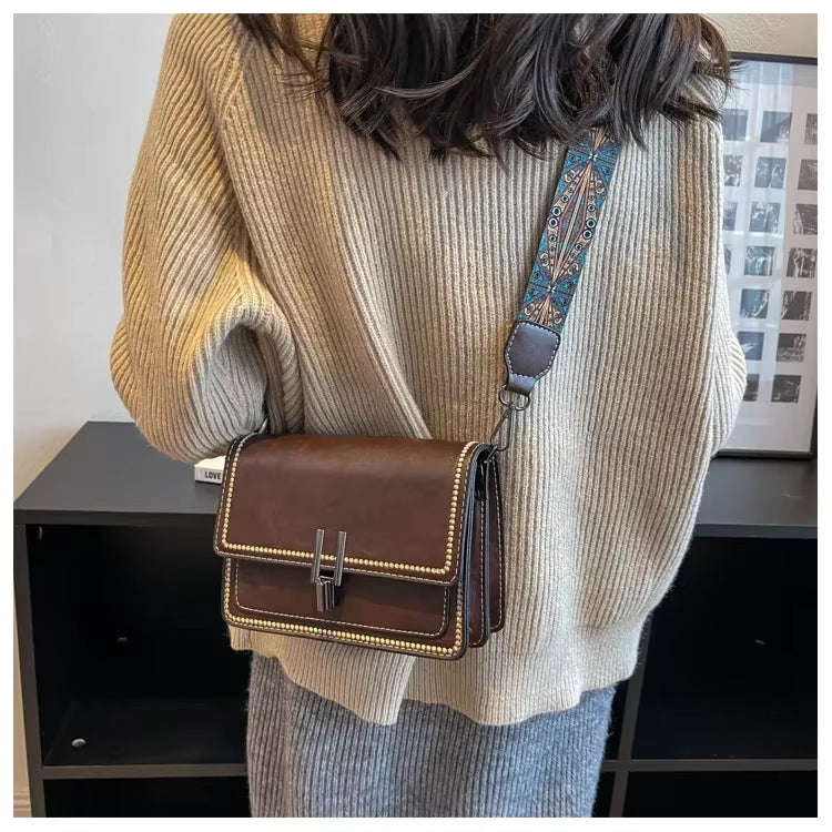 Donna con maglione beige indossa borsa a tracolla marrone con dettagli decorativi. Accessorio moda elegante, perfetto per look casual e autunnali.