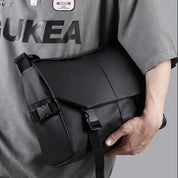 Borsa a tracolla nera impermeabile, design moderno, chiusura a fibbia, indossata da una persona. Accessorio moda unisex, ideale per viaggi e lavoro.