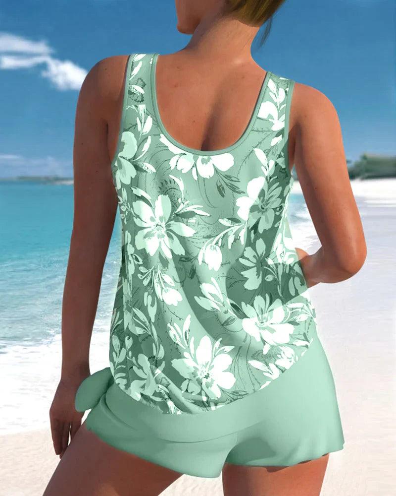 Donna in costume da bagno verde con stampa floreale bianca, spiaggia tropicale sullo sfondo, moda mare estiva, abbigliamento da spiaggia elegante.