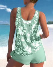 Donna in costume da bagno verde con stampa floreale bianca, spiaggia tropicale sullo sfondo, moda mare estiva, abbigliamento da spiaggia elegante.