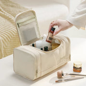 Borsa da toilette beige aperta su tavolo, contenente flaconi di cosmetici e accessori trucco. Design elegante, ideale per viaggi e organizzazione.