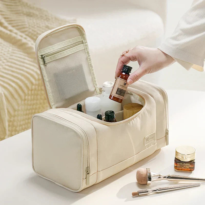 Borsa da toilette beige aperta su tavolo, contenente flaconi di cosmetici e accessori trucco. Design elegante, ideale per viaggi e organizzazione.