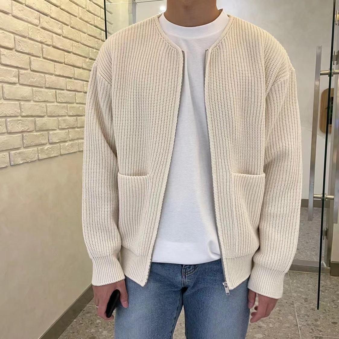 Uomo con cardigan beige a maglia, tasche frontali, indossa jeans blu e maglietta bianca. Moda casual, abbigliamento autunnale, stile urbano.