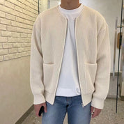 Uomo con cardigan beige a maglia, tasche frontali, indossa jeans blu e maglietta bianca. Moda casual, abbigliamento autunnale, stile urbano.