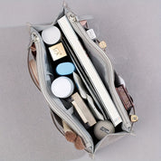 Borsa organizer grigia aperta vista dall'alto, contenente cosmetici, libri e accessori. Ideale per organizzazione e viaggio.