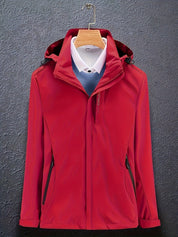 Giacca rossa impermeabile con cappuccio, appesa su gruccia, sopra camicia bianca e maglione blu. Abbigliamento outdoor elegante e funzionale.