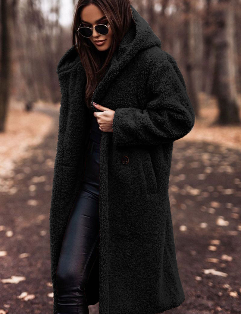 Donna con cappotto in pelliccia sintetica nero, occhiali da sole, pantaloni in pelle, in un parco autunnale. Moda autunno inverno, stile elegante.
