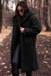 Donna con cappotto in pelliccia sintetica nero, occhiali da sole, pantaloni in pelle, in un parco autunnale. Moda autunno inverno, stile elegante.