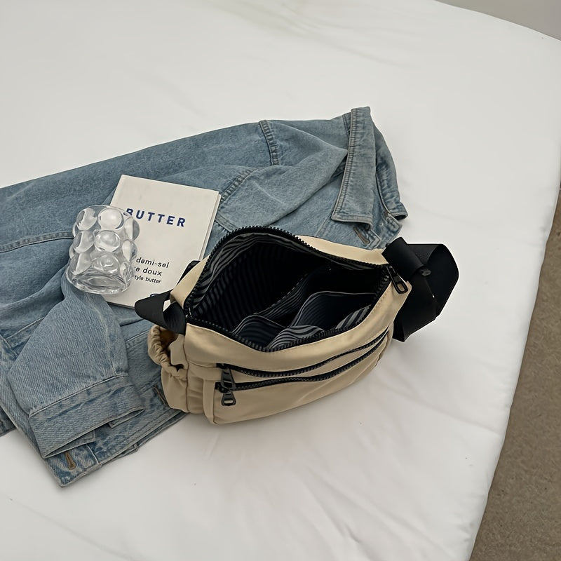 Marsupio beige aperto su giacca di jeans, con libro e portaghiaccio trasparente su letto bianco. Accessori moda casual, stile urbano.