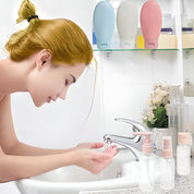 Donna che si lava il viso in bagno moderno, flaconi da viaggio colorati sullo sfondo. Cura della pelle, routine di bellezza, igiene personale.