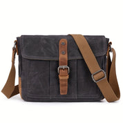 Borsa a tracolla in tela nera con cinturino regolabile marrone, chiusura a fibbia in pelle. Design casual, ideale per uomo e donna.