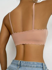 Donna indossa reggiseno senza cuciture color nude con spalline sottili e bordo ondulato, abbinato a jeans a vita alta. Moda intima femminile elegante.