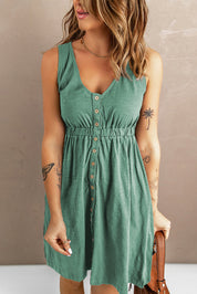 Donna con abito estivo verde, bottoni frontali, tatuaggi visibili su braccia, capelli ondulati, sfondo neutro. Moda femminile casual elegante.