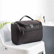 Borsa da toilette nera su sedia bianca, con zip multiple, ideale per viaggi. Design compatto e resistente, perfetta per organizzare accessori bagno.