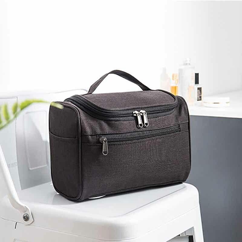 Borsa da toilette nera su sedia bianca, con zip multiple, ideale per viaggi. Design compatto e resistente, perfetta per organizzare accessori bagno.
