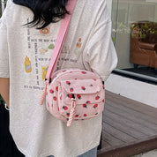 Donna con borsa a tracolla rosa con stampa fragole, indossa maglietta beige con illustrazioni. Moda casual estiva, accessori femminili trendy.