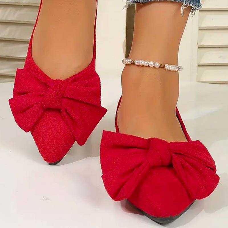 Scarpe rosse da donna con fiocco grande, punta affusolata, indossate con cavigliera di perle. Scarpe eleganti, moda femminile, calzature trendy.
