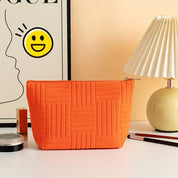Borsa cosmetica arancione su tavolo bianco, lampada moderna e poster artistico. Design trapuntato, accessorio moda, organizzazione trucco.