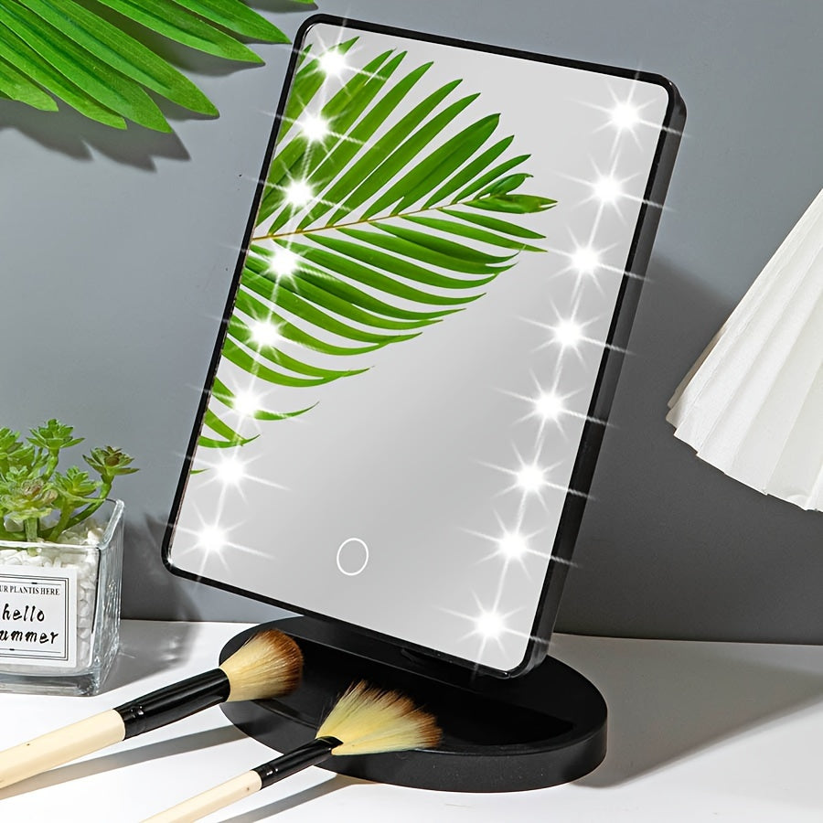 Specchio cosmetico LED rettangolare con foglia verde riflessa, base nera, circondato da pennelli trucco e pianta decorativa. Perfetto per make-up.