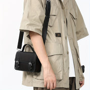 Uomo con camicia beige indossa borsa a tracolla nera in pelle, design elegante e moderno, ideale per moda urbana e casual.
