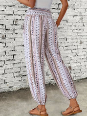 Pantaloni estivi donna a righe bianche e nere, motivo etnico, elastico in vita, tasche laterali, indossati con sandali marroni, sfondo muro bianco.