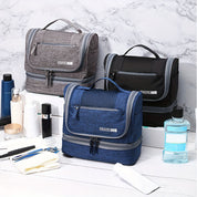 Tre beauty case da viaggio in tessuto, colori grigio, nero e blu, con zip e manico, su sfondo marmo. Accessori da bagno inclusi.