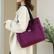 Borsa a tracolla viola in nylon, design elegante e moderno, con manici neri, indossata da una donna. Accessorio moda versatile e resistente.