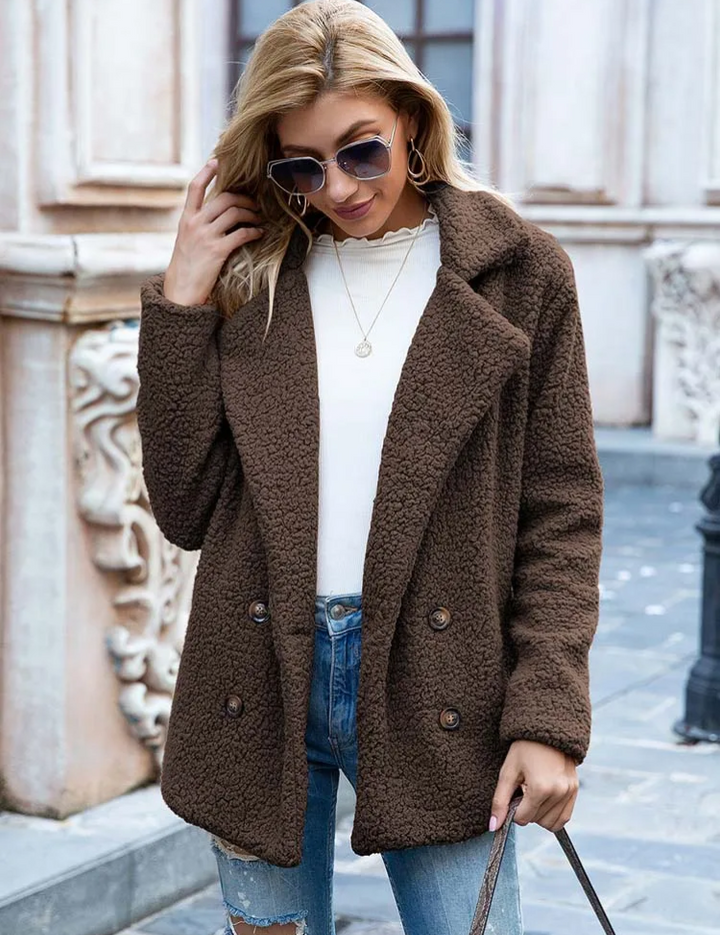 Donna con cappotto marrone in lana bouclé, occhiali da sole, maglia bianca e jeans strappati. Moda autunnale, abbigliamento casual elegante.