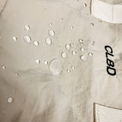 Giacca impermeabile beige con gocce d'acqua, logo CLBD ricamato. Tessuto resistente all'acqua, ideale per attività all'aperto.